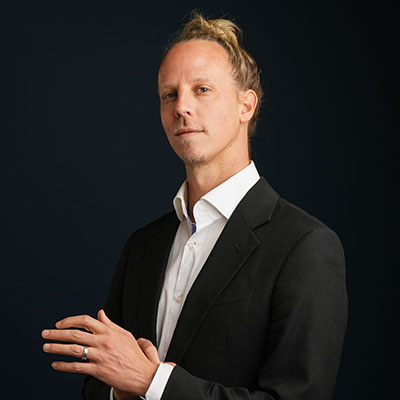 Dr. Geoffrey Dean wearing black suit and white shirt with blonde bun