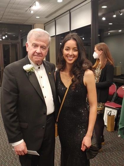 Catherine "Kitty" Fields, a young woman with long dark hair and wearing a dark sparkly dress (right), stands with Mason professor and composer Mark Camphouse (left), an older white man with white hair wearing a dark suit and white shirt.
