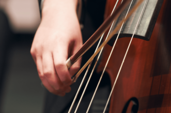 zoomed in photo of hand holding a string bow and playing a stringed instrument