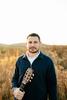 Matt Trkula holding guitar in a field wearing blue sweater
