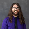 Prof. John Helig with long brown hair wearing glasses, a purple shirt and polka dotted tie