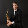 Dr. Connor Mikula wearing a black suit holding his saxophone.