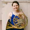 Dr. Caroline Steiger in a blue jumpsuit holding her French Horn